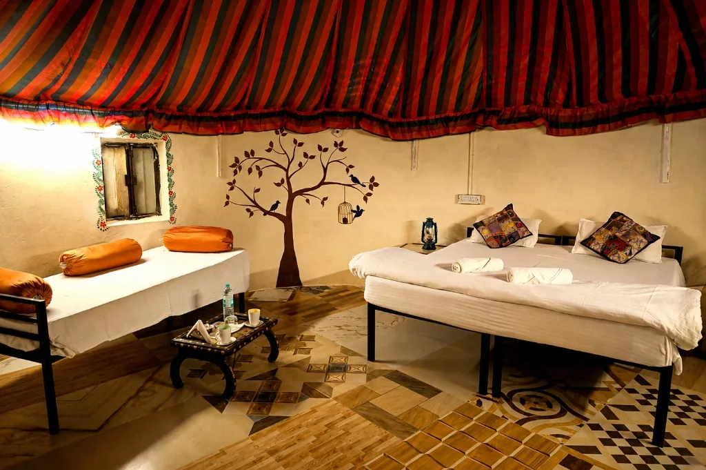 Authentic Mud Cottage interior with double bed, daybed, painted tree mural and patterned ceiling canopy