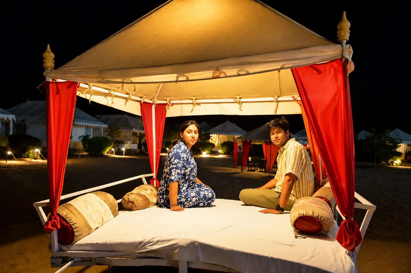 Guests relaxing on an illuminated open-air canopy lounge bed at night