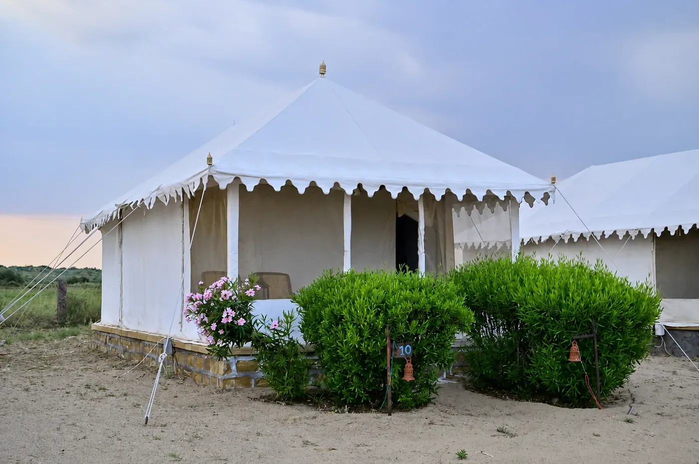 White Swiss tent exterior on stone foundation surrounded by desert flowering shrubs