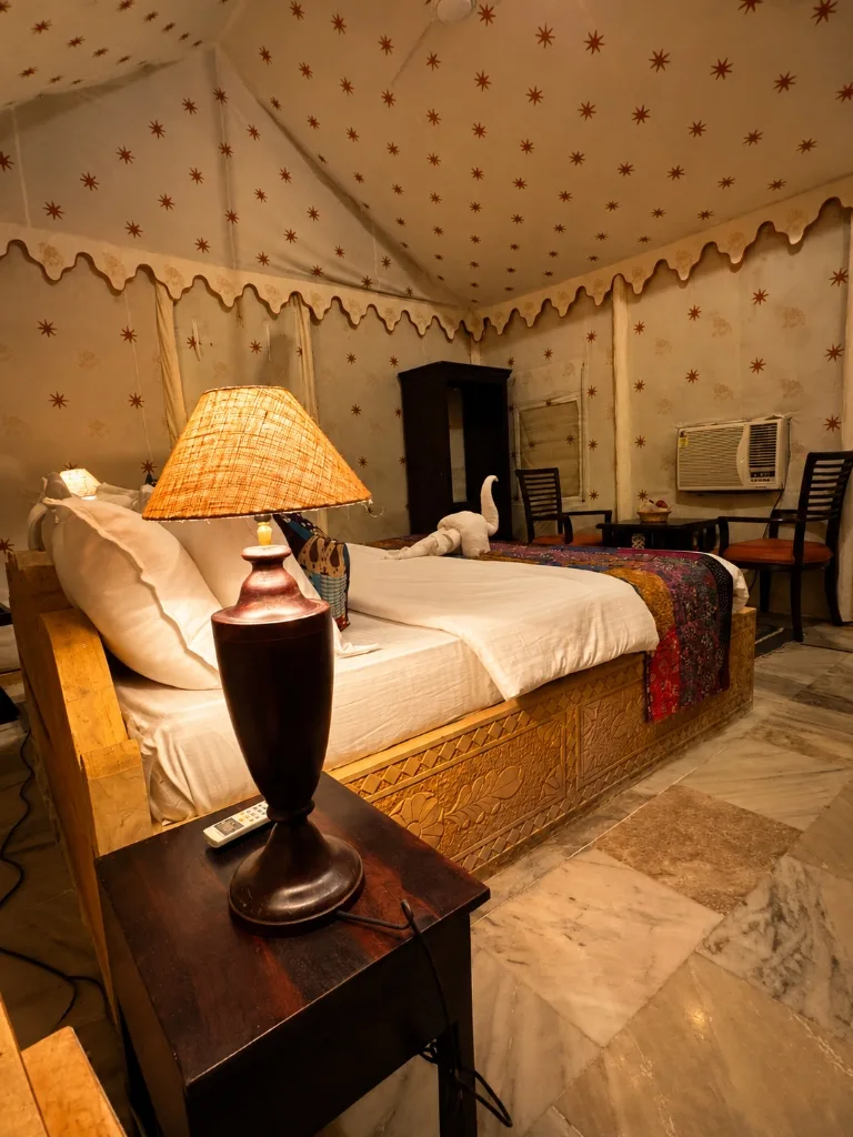 Warm night lighting in Super Deluxe tent with bedside lamp, air conditioner and carved wooden bed